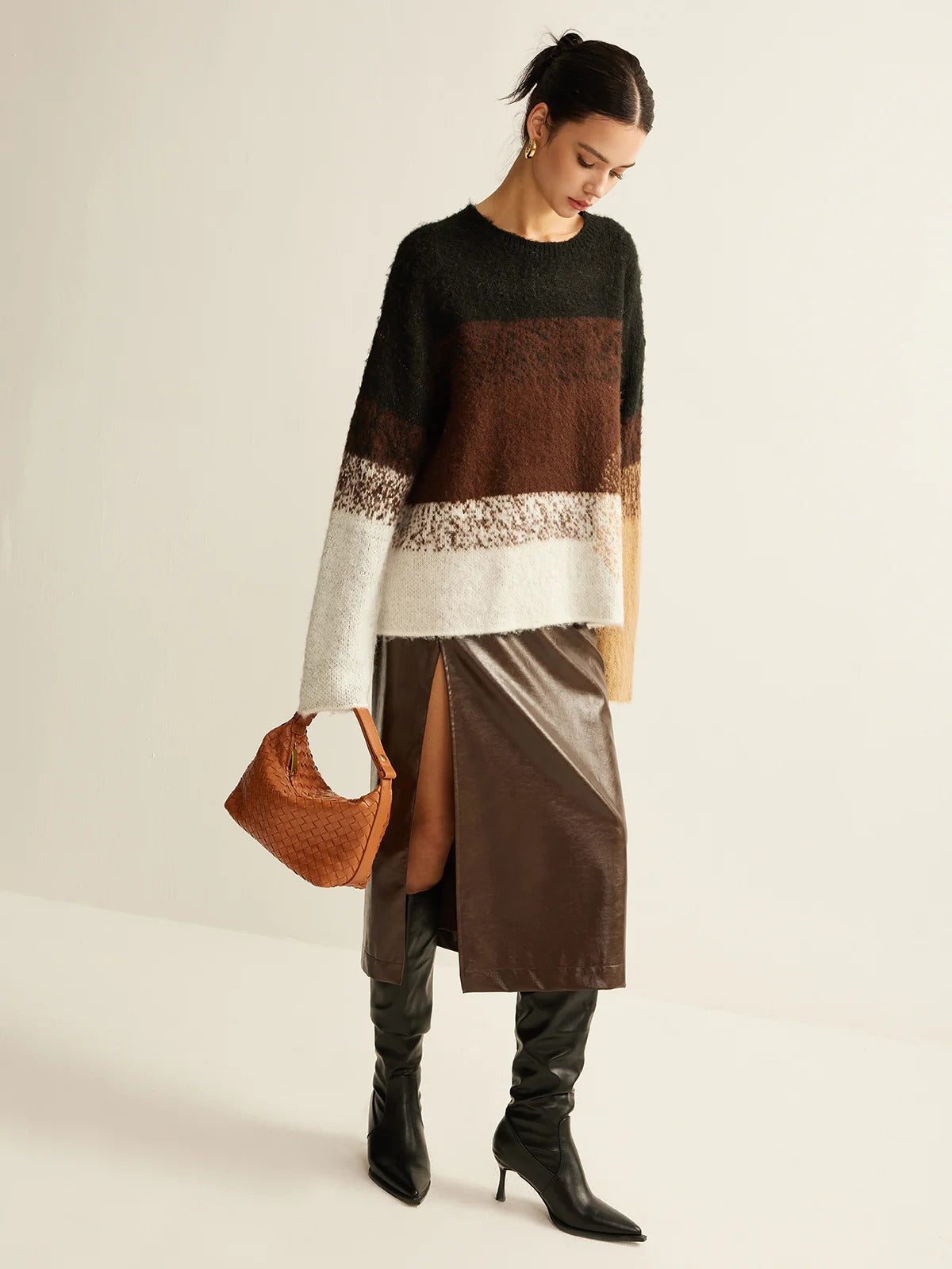 Woman wearing a brown and white sweater with a skirt, holding a brown handbag on a plain background