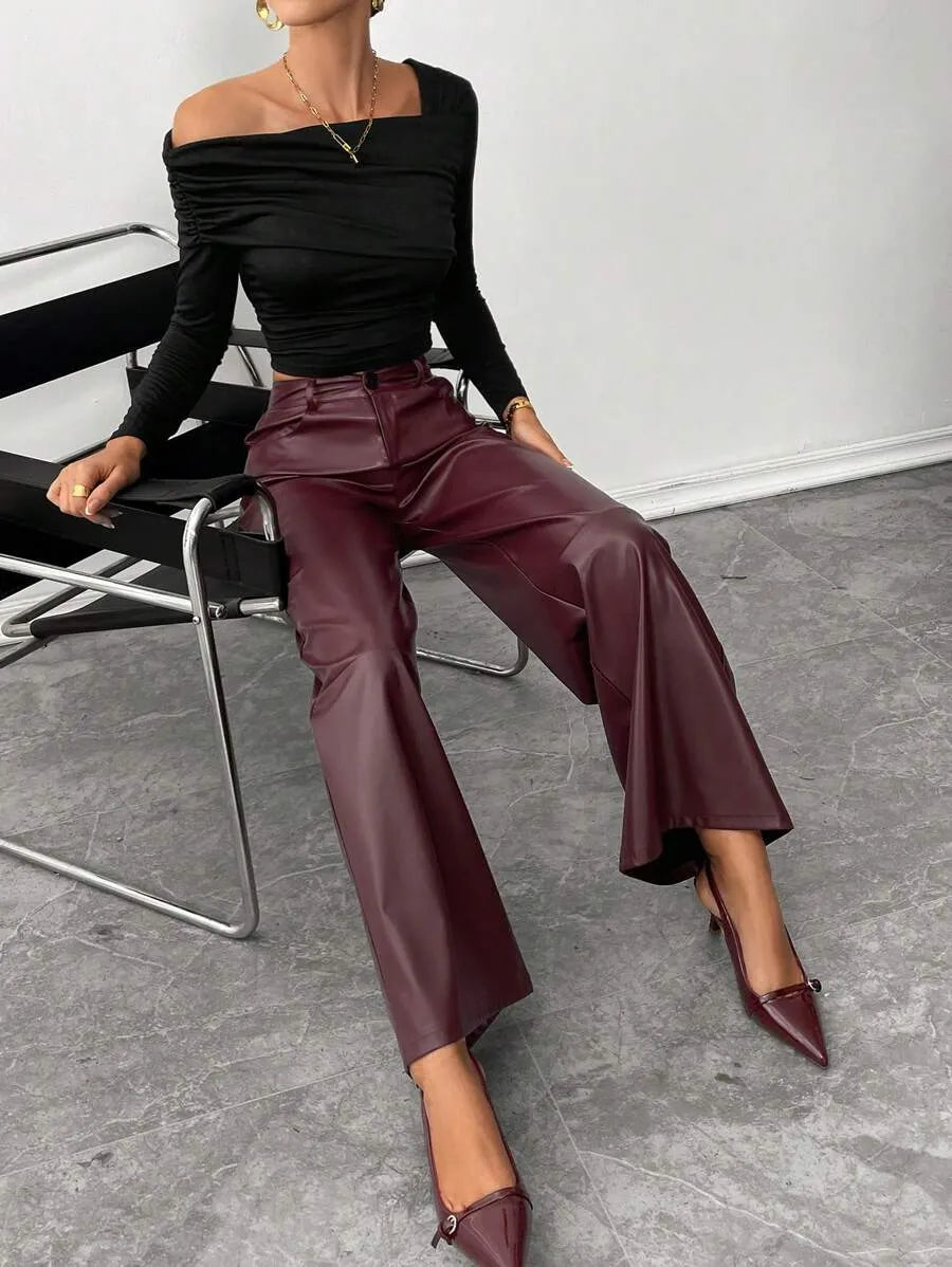 Person wearing a black off-shoulder top and burgundy pants sitting on a chair.