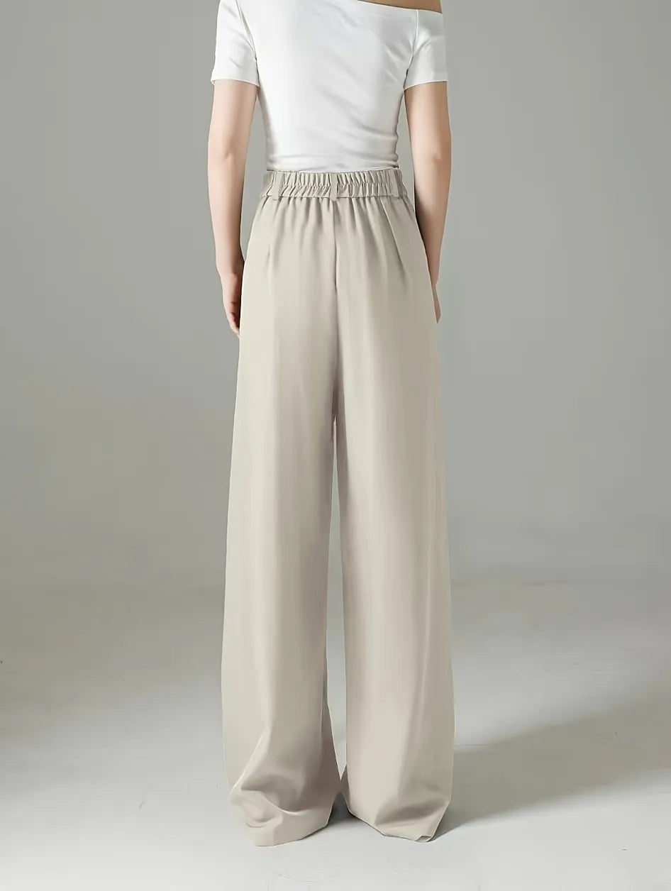 Person wearing beige wide-leg pants and a white top on a plain background