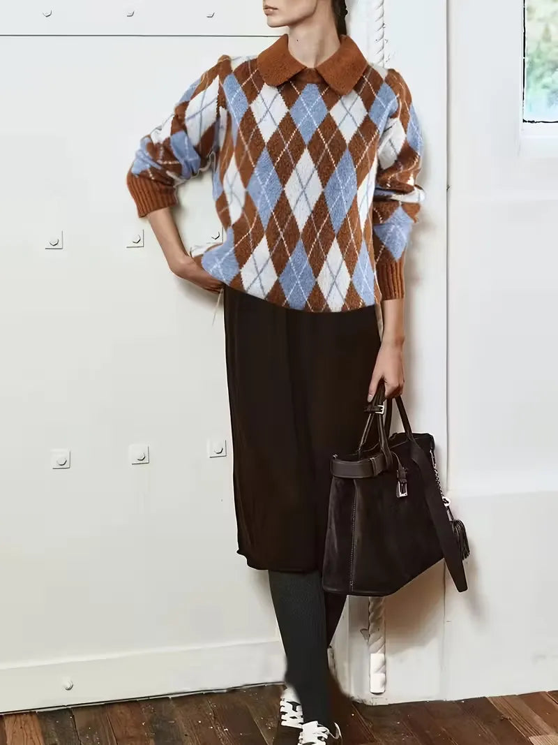 Person wearing a brown and blue argyle sweater with a black handbag against a white wall.