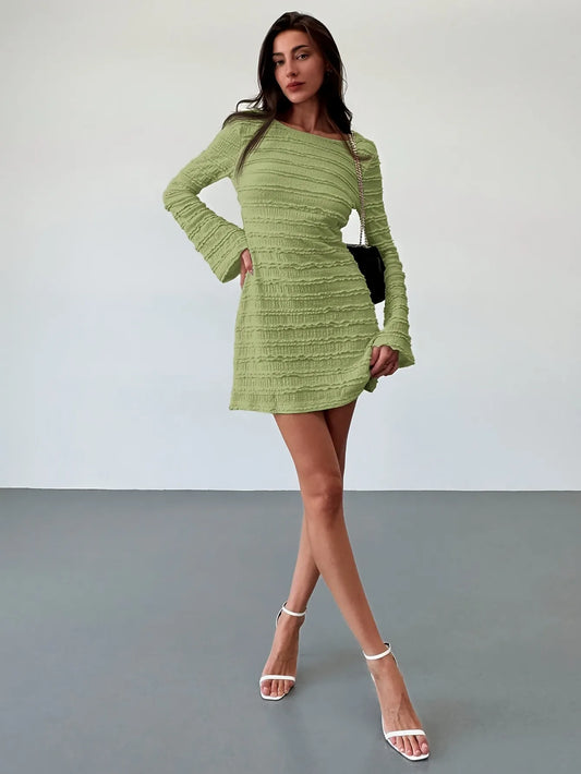 Woman wearing a green dress with long sleeves against a plain background