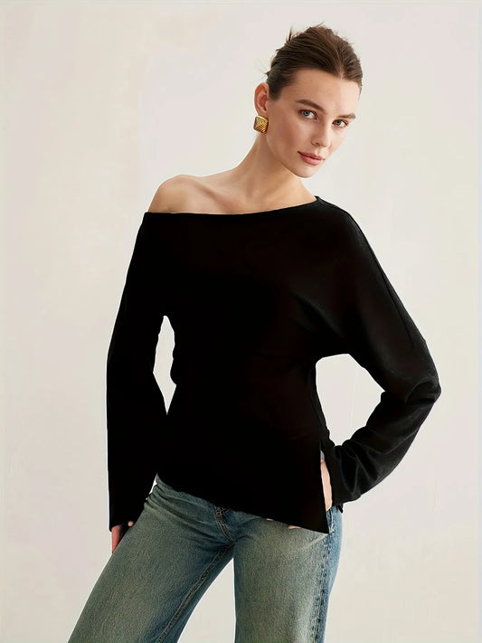Woman wearing a black off-the-shoulder long-sleeve top paired with light blue jeans. The top has a relaxed fit and an asymmetrical neckline, styled with gold statement earrings and a sleek updo for an elegant minimalist look.