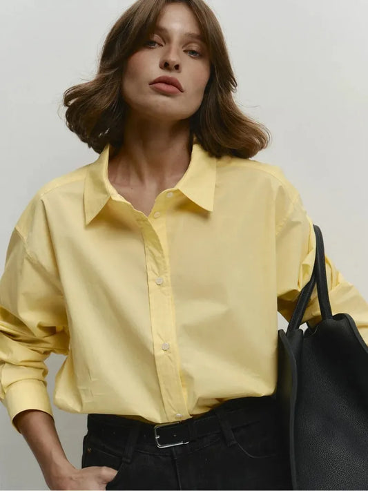 Woman wearing a yellow shirt holding a black handbag against a plain background