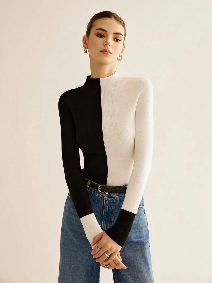 Person wearing a black and white long-sleeve top with blue jeans on a plain background