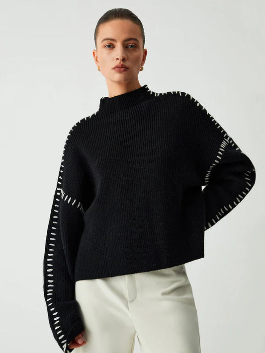 Person wearing a black sweater with white trim on a plain background