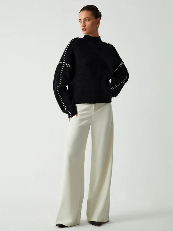 Person wearing a black sweater with white trim and white pants on a light gray background