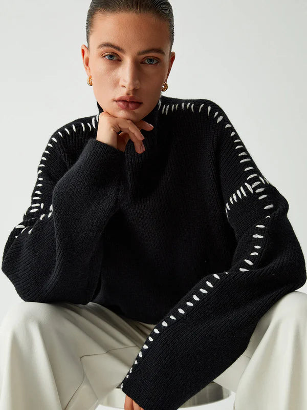 Person wearing a black sweater with white trim sitting against a plain background