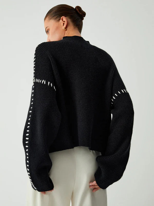 Person wearing a black sweater with white accents on a plain background