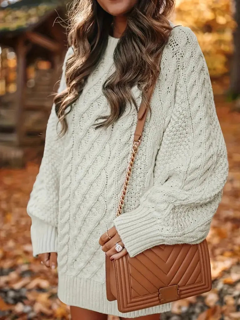Person wearing a cable knit sweater with a brown handbag in an autumn setting