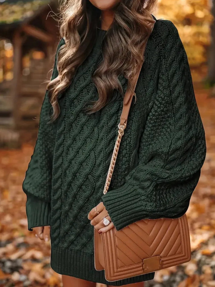 Person wearing a green cable knit sweater with a brown handbag on a blurred autumn background