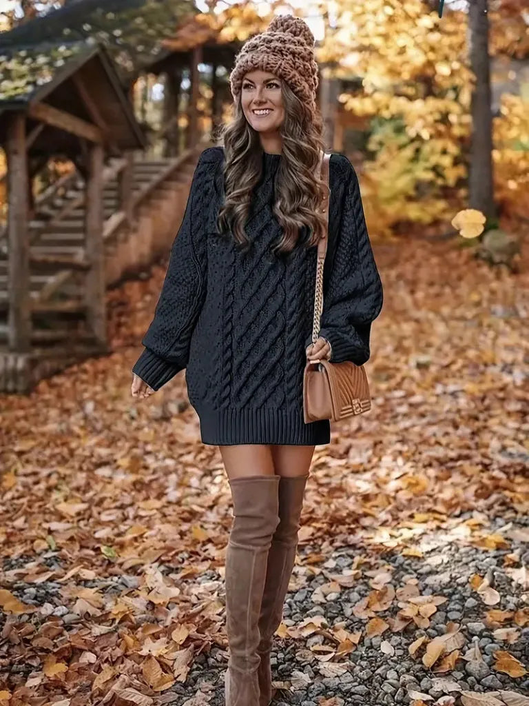 Woman in a dark sweater dress and brown knee-high boots standing in autumn leaves.