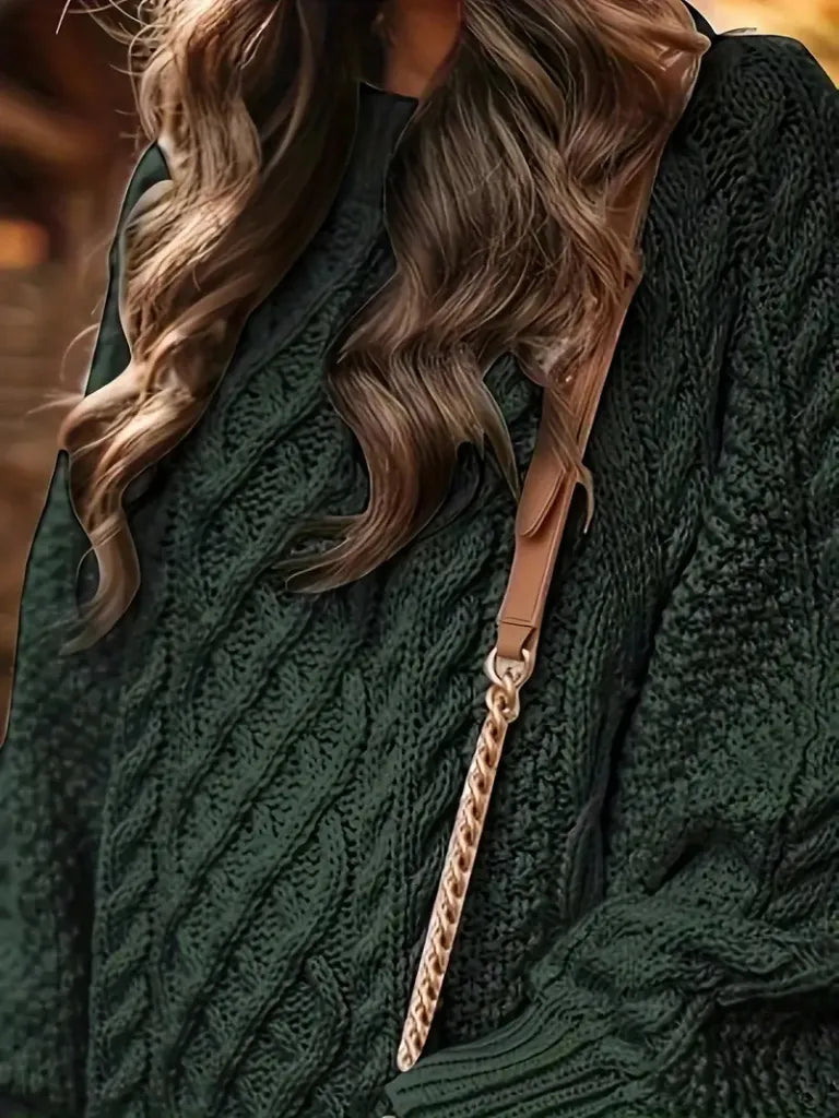 Person wearing a green cable knit sweater with a brown leather bag strap over shoulder