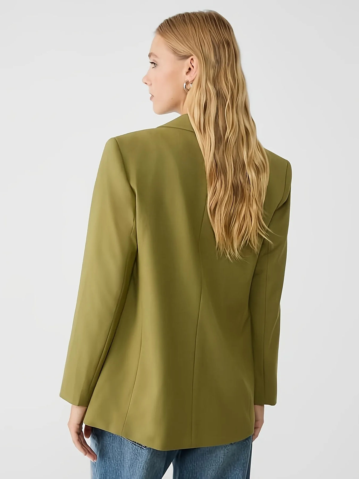 Woman wearing a green jacket with a tailored fit, layered over a cream long-sleeve top with black contrast wavy stitching, paired with high-waisted blue jeans. The look is completed with hoop earrings and a sleek bun hairstyle for a modern minimalist aesthetic.