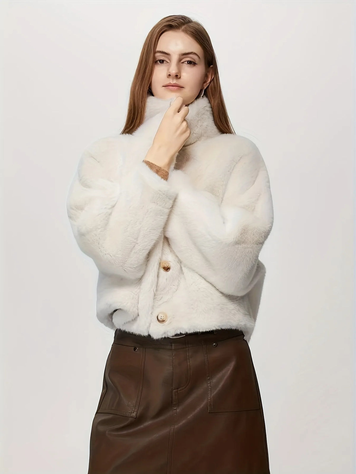 Woman wearing a white textured sweater with brown leather skirt on a light background