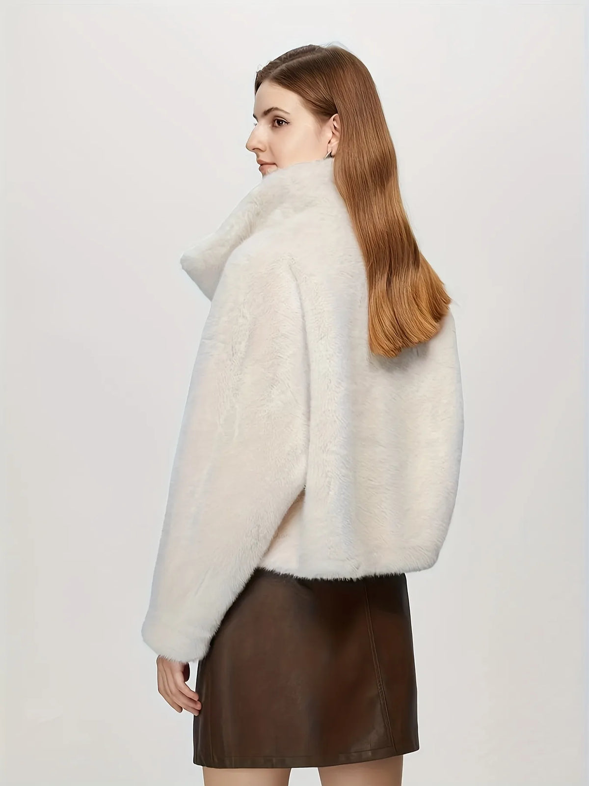 Woman wearing a white fur coat and brown leather skirt on a light gray background