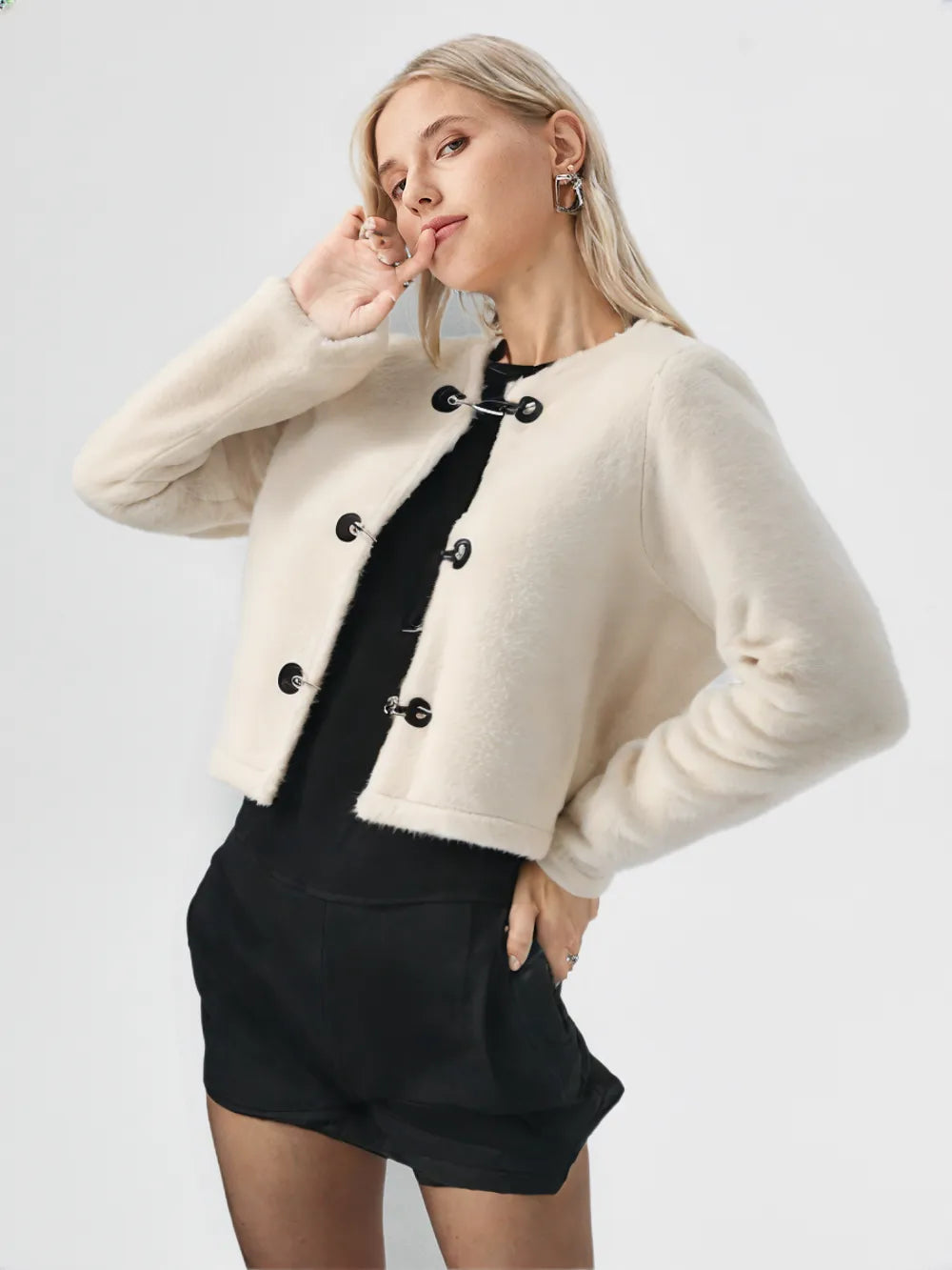 Woman wearing a beige cropped jacket with black buttons on a white background