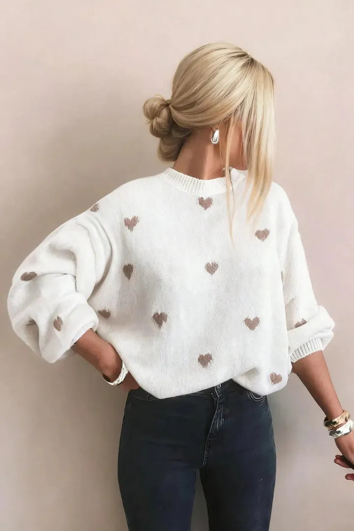 Person wearing a white sweater with heart patterns against a beige background