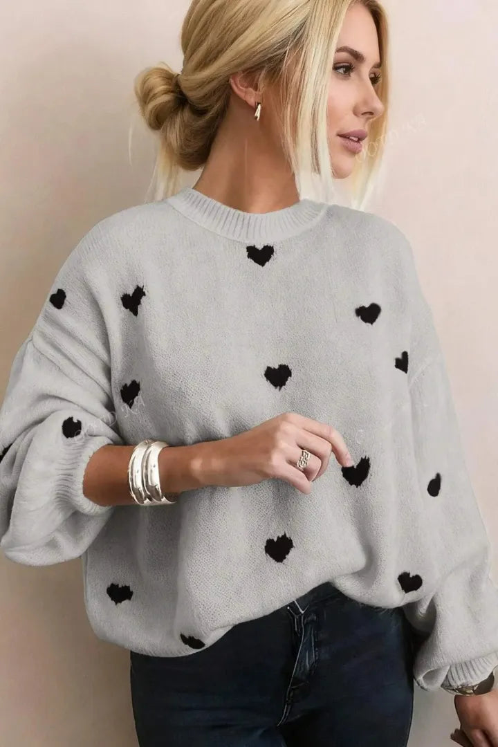 Woman wearing a gray sweater with black heart patterns against a plain background
