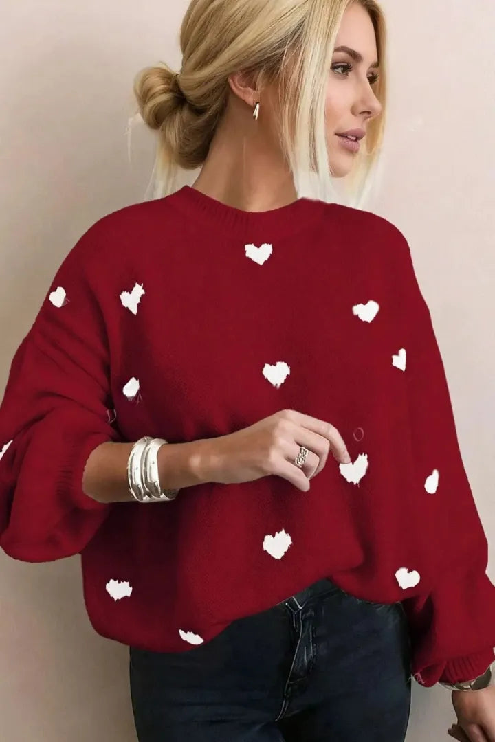 Woman wearing a red sweater with white heart patterns against a plain background