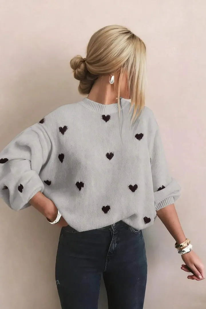 Person wearing a light gray sweater with black heart patterns against a beige background