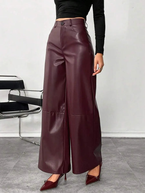 Person wearing maroon leather wide-leg pants with a black top and shoes in a minimalistic setting.