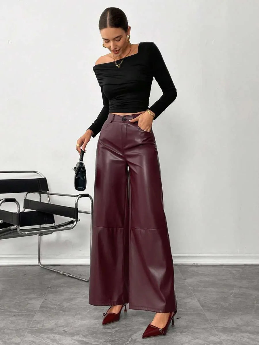 Woman wearing a black top and maroon wide-leg pants standing against a white wall.