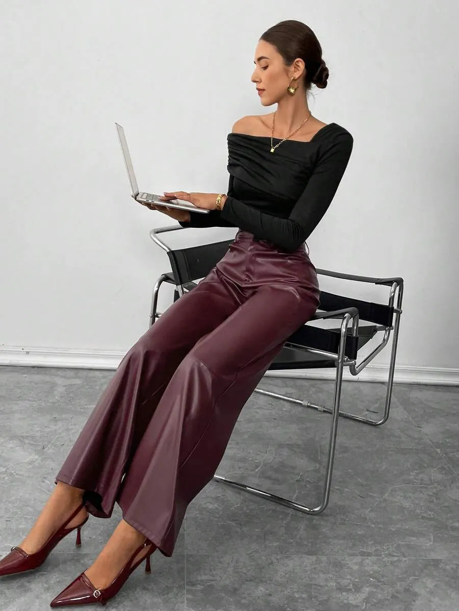 Woman sitting on a chair using a laptop, wearing a black top and burgundy pants.