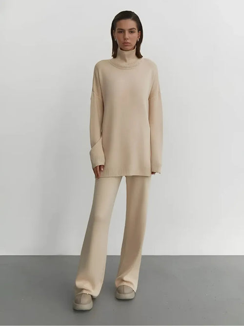 Woman wearing a beige turtleneck sweater and pants on a plain background