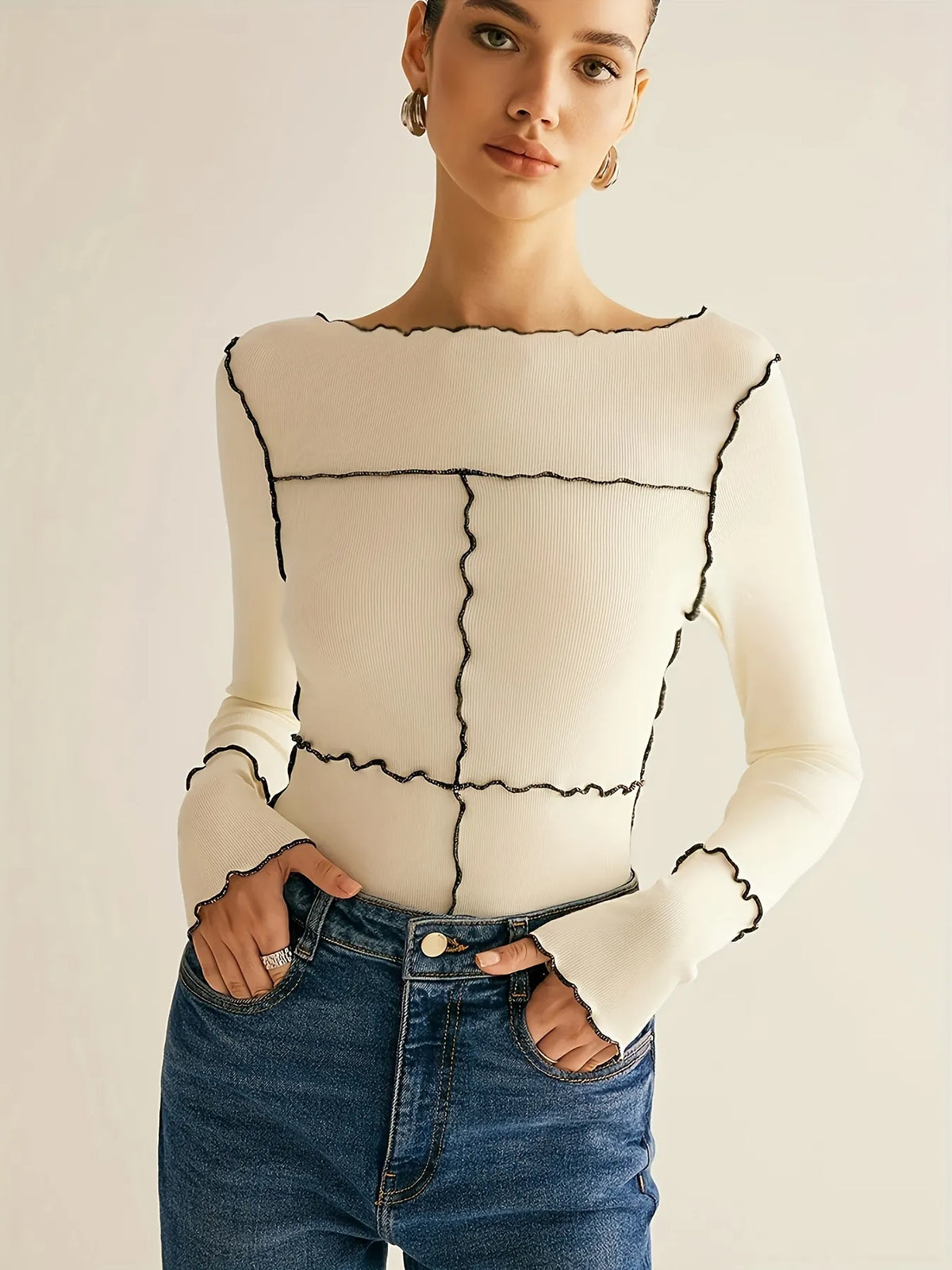 Woman wearing a cream sweater with black geometric patterns and blue jeans on a plain background