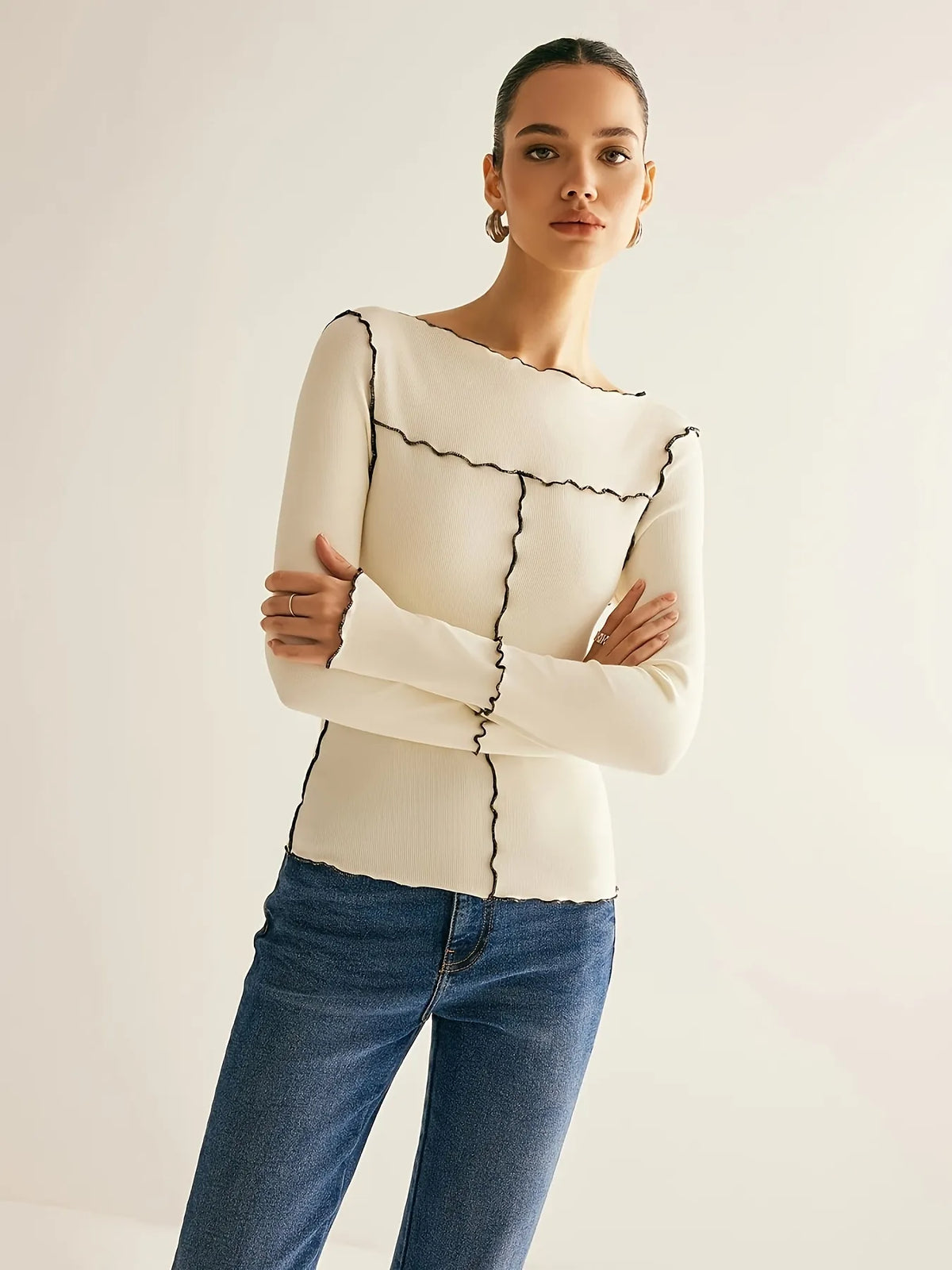 Woman wearing a cream sweater with black pattern and blue jeans on a plain background