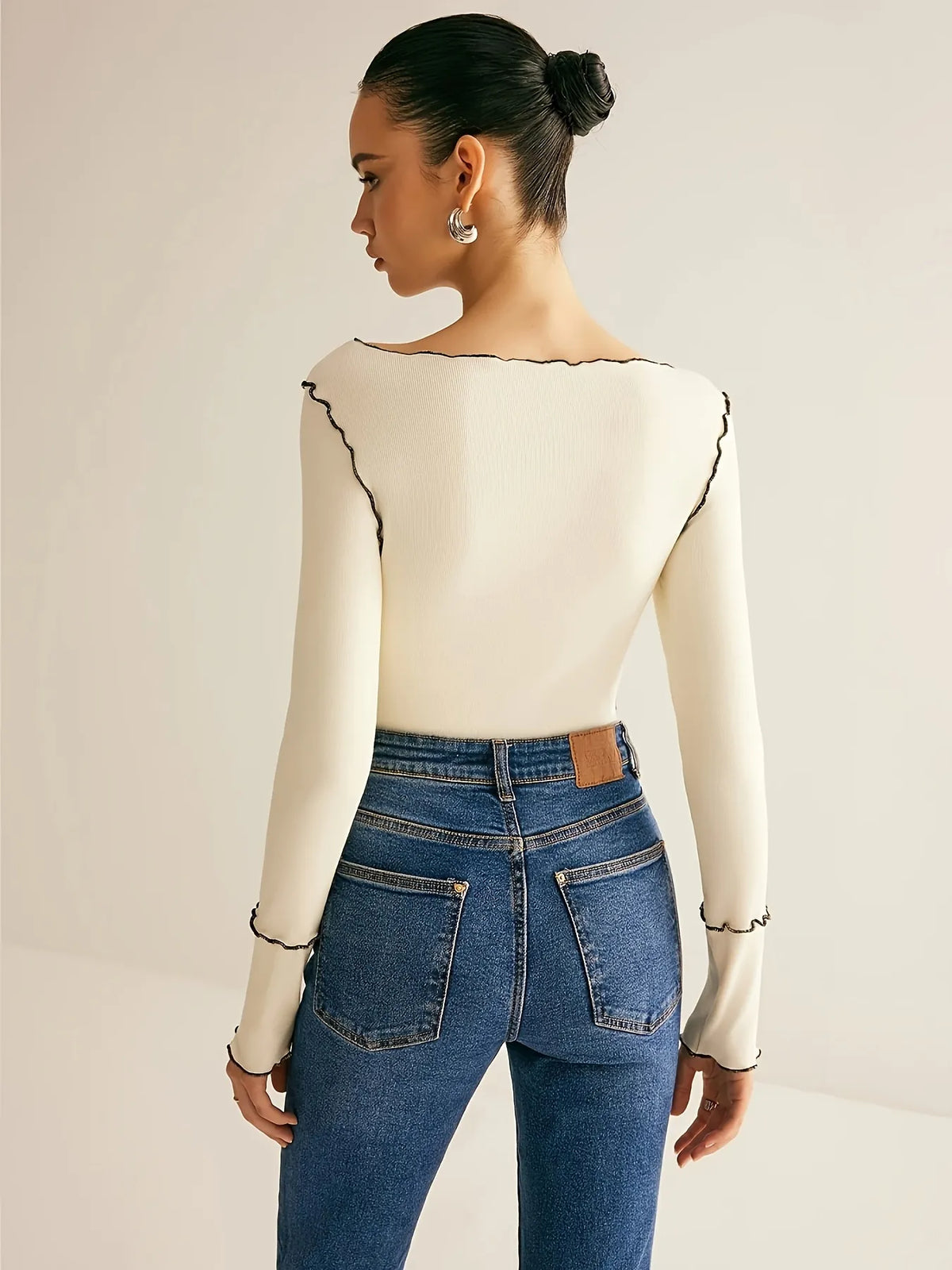Person wearing a cream long-sleeve top with black trim and blue jeans on a plain background