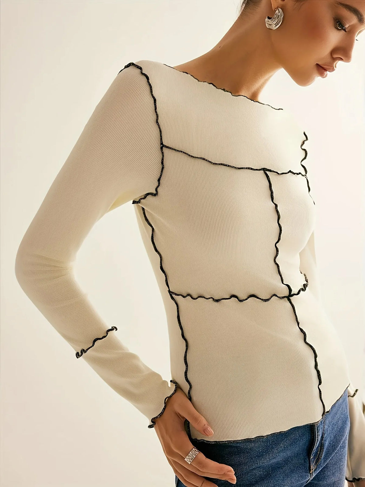 Woman wearing a beige sweater with black trim on a plain background