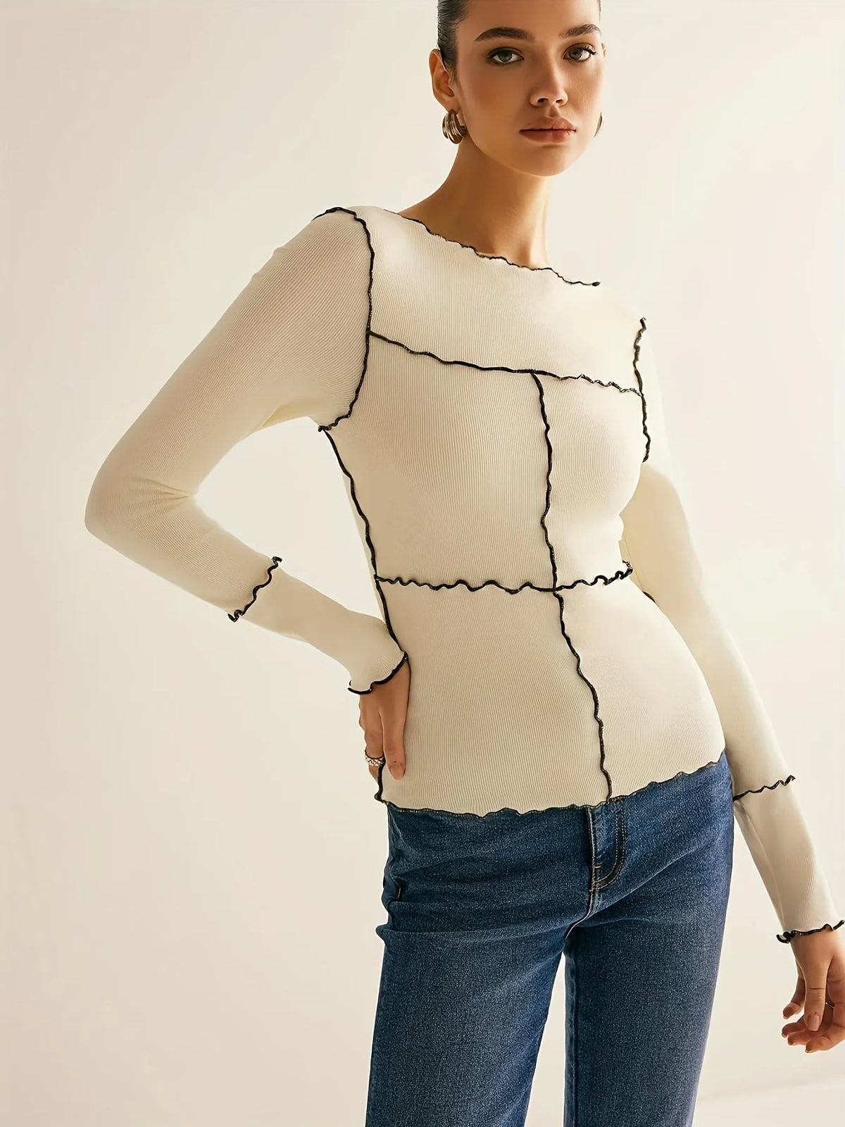 Woman wearing a beige long-sleeve top with black geometric patterns and blue jeans on a light background