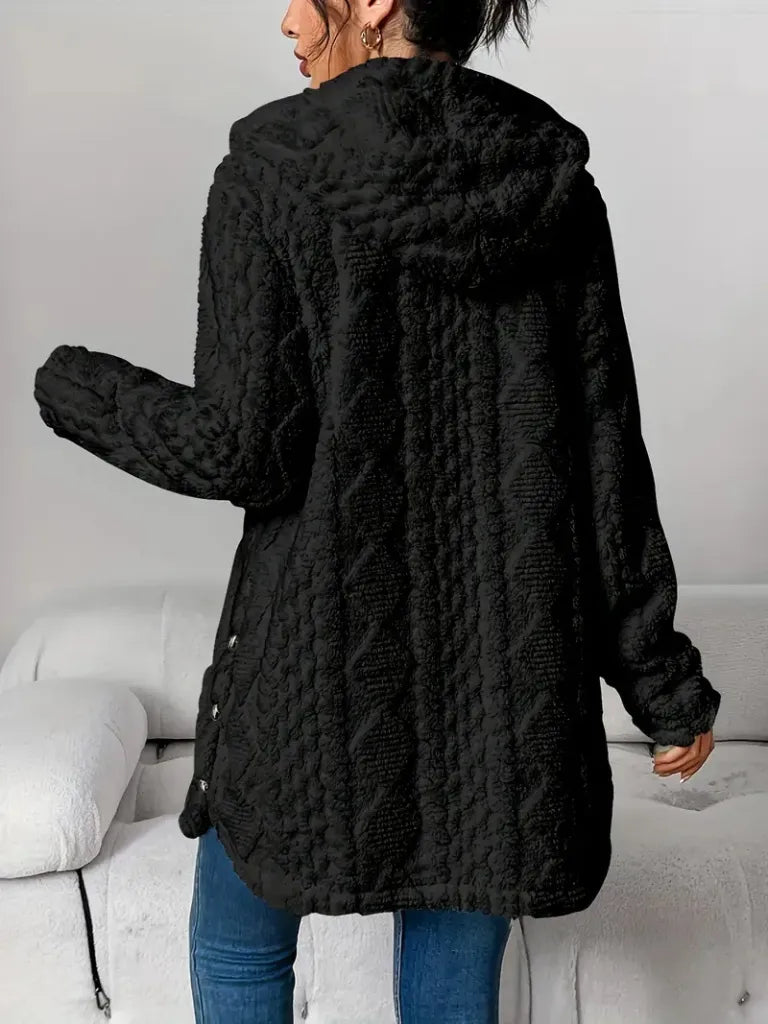 Person wearing a black textured coat in a minimal indoor setting