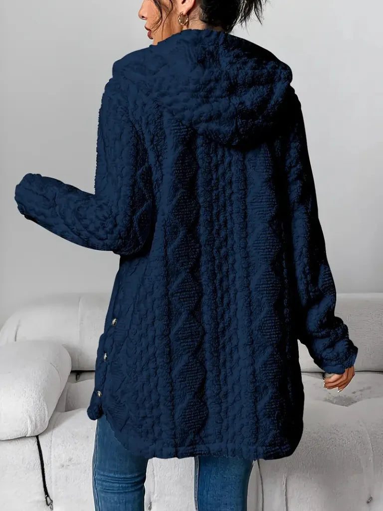 Person wearing a navy blue textured coat in a minimal indoor setting
