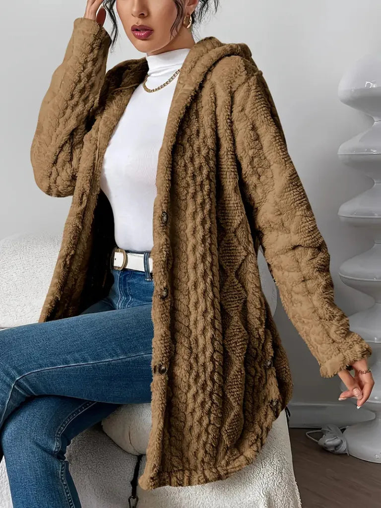 Person wearing a brown textured cardigan over a white top and blue jeans, sitting on a white surface.