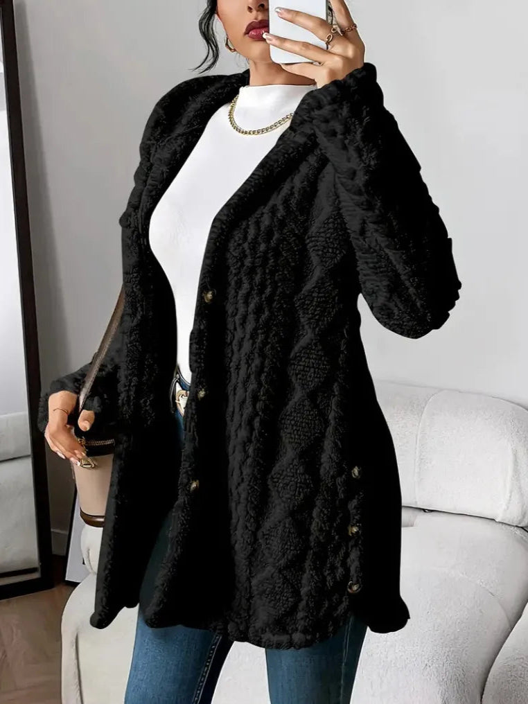 Person wearing a black textured cardigan over a white top and blue jeans, holding a phone.