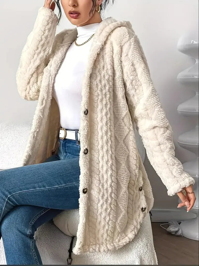 Person wearing a cream-colored cardigan with a white shirt and blue jeans indoors.