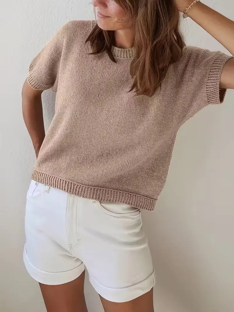 Person wearing a beige knit sweater and white shorts against a plain background