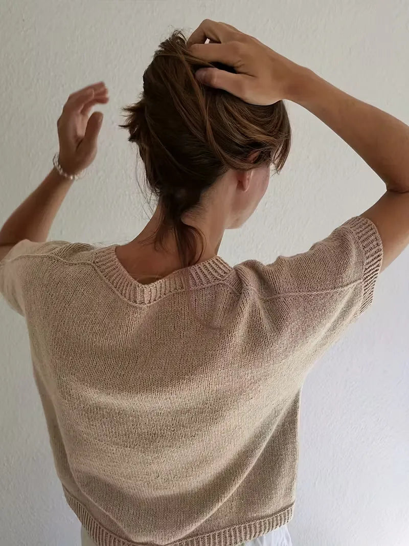 Person wearing a beige knit sweater against a plain background