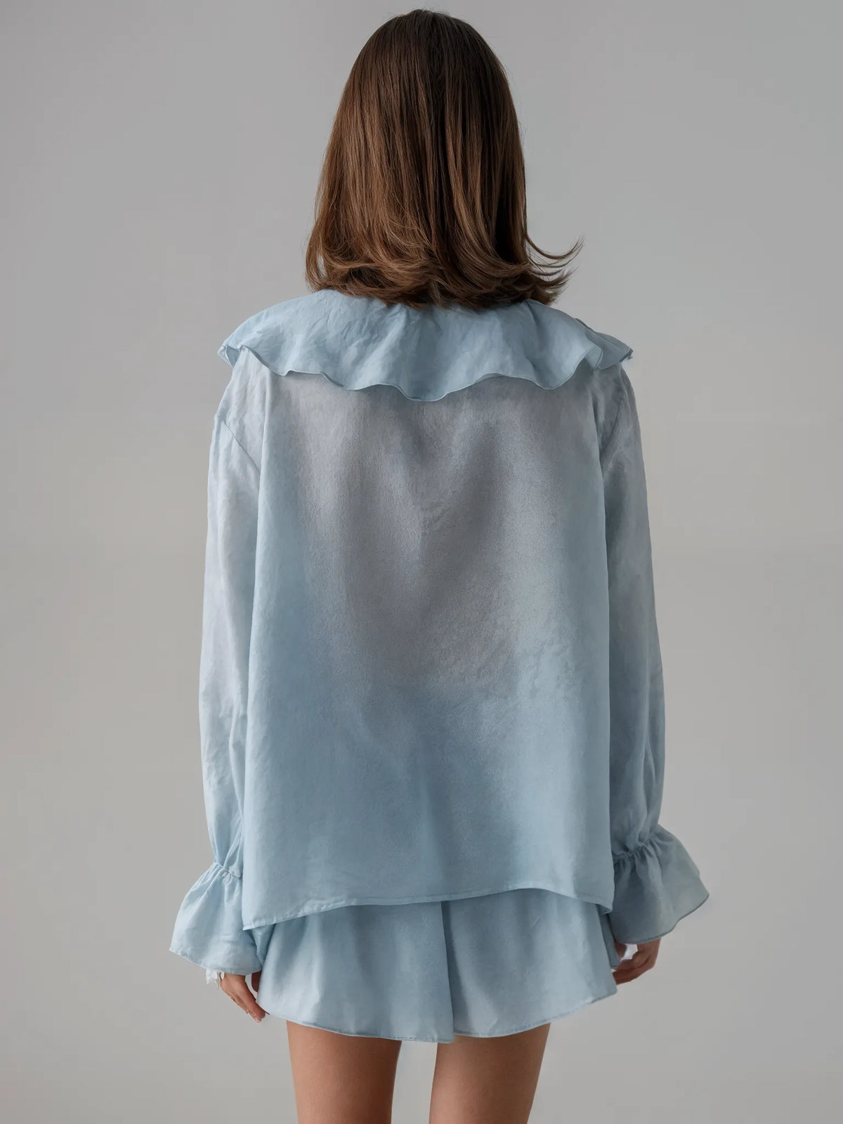 Light blue blouse with ruffled collar and cuffs worn by a person on a plain background