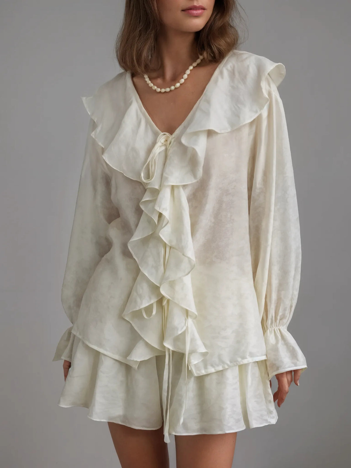 Woman wearing a white ruffled blouse and shorts set against a gray background