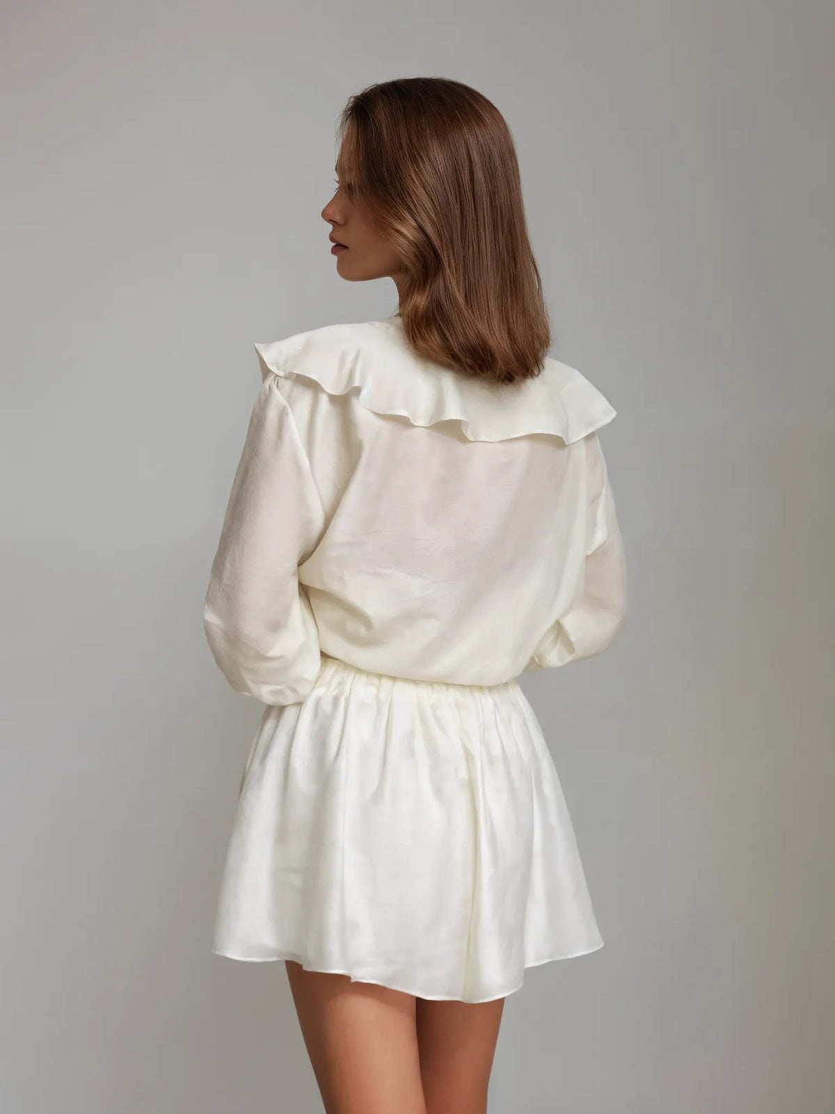 Woman wearing a white dress with ruffled collar against a gray background