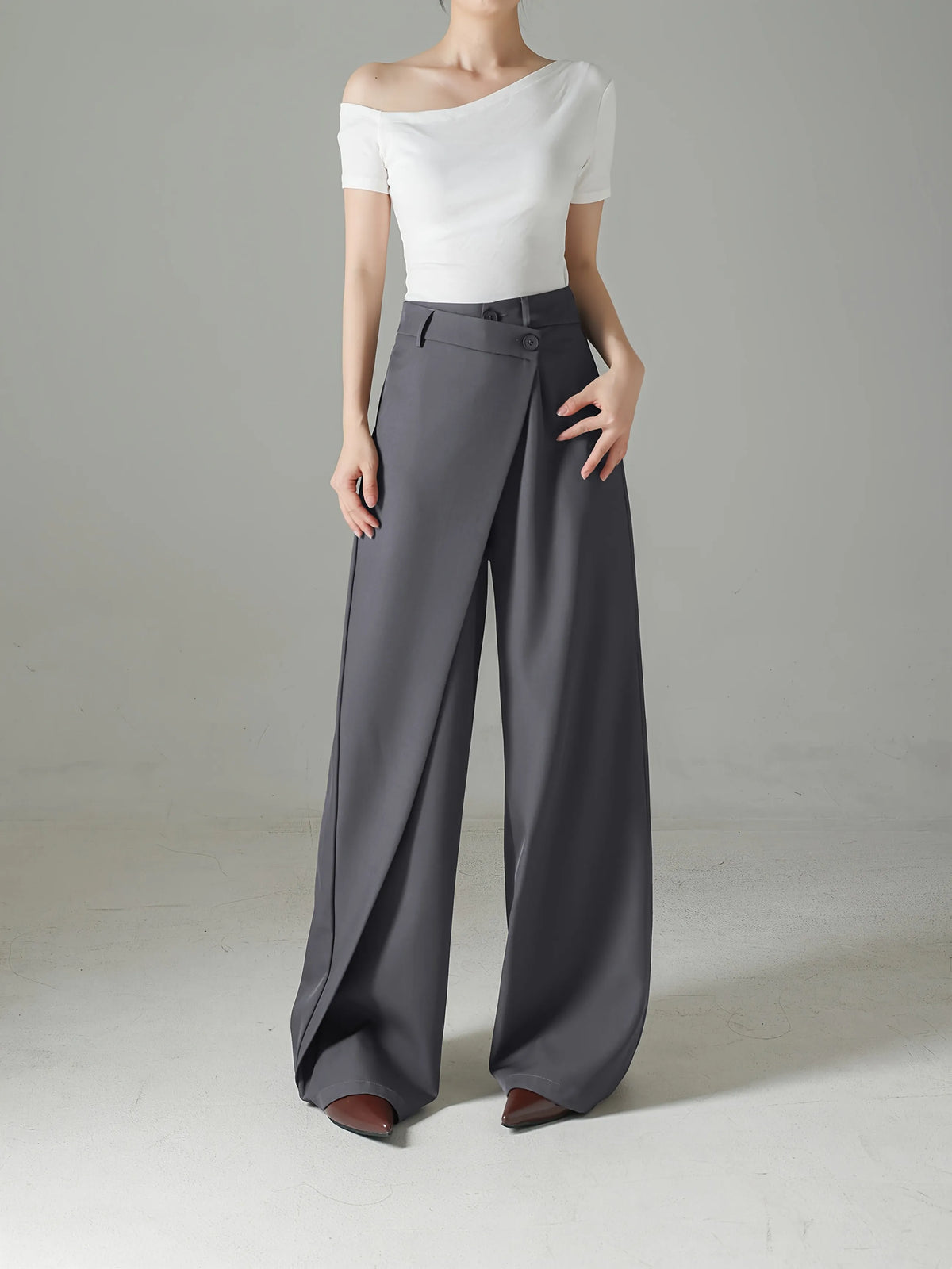 Person wearing a white off-shoulder top and gray wide-leg pants on a plain background