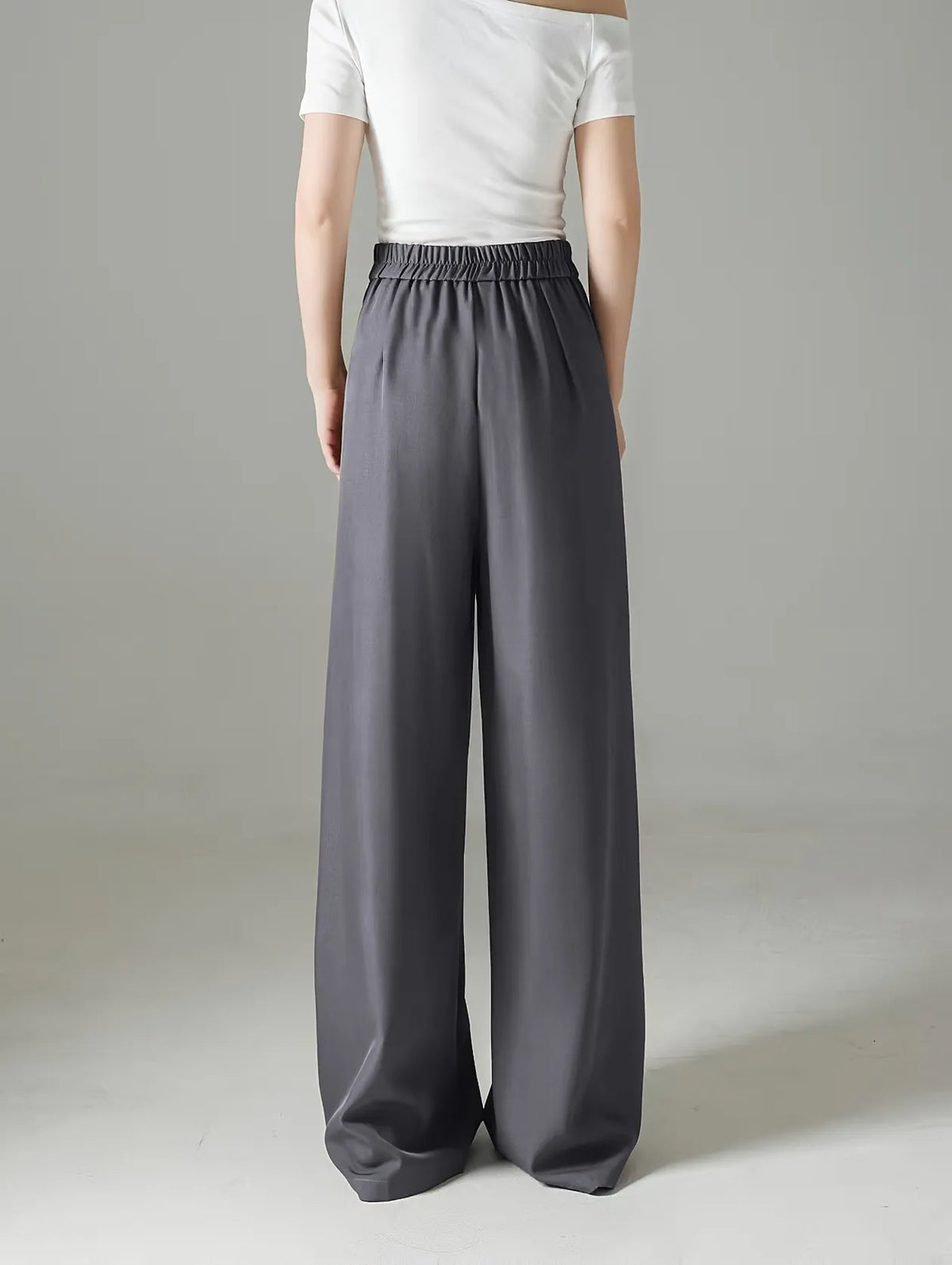 Person wearing gray wide-leg pants and a white top on a plain background