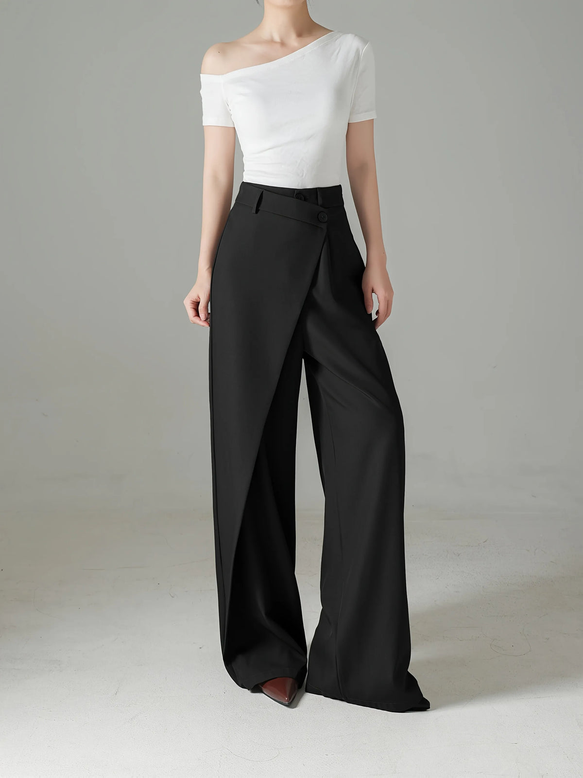 Person wearing a white off-shoulder top and black wide-leg pants on a plain background