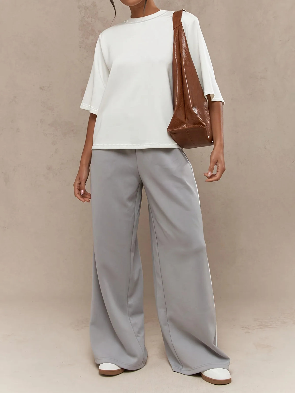 Person wearing a white top and gray pants with a brown bag on a beige background