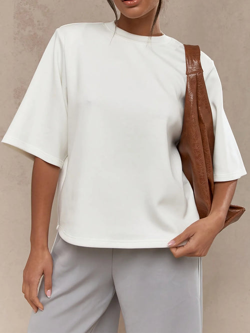 Person wearing a white top and light gray pants with a brown leather bag on a beige background