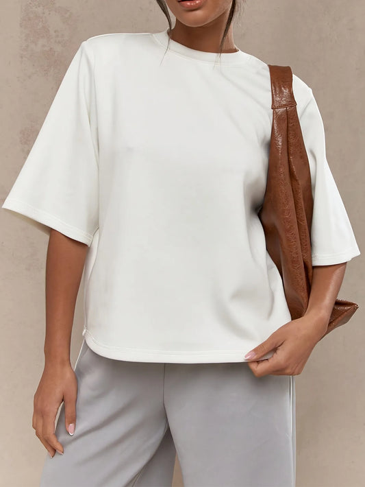 Person wearing a white top and light gray pants with a brown leather bag on a beige background