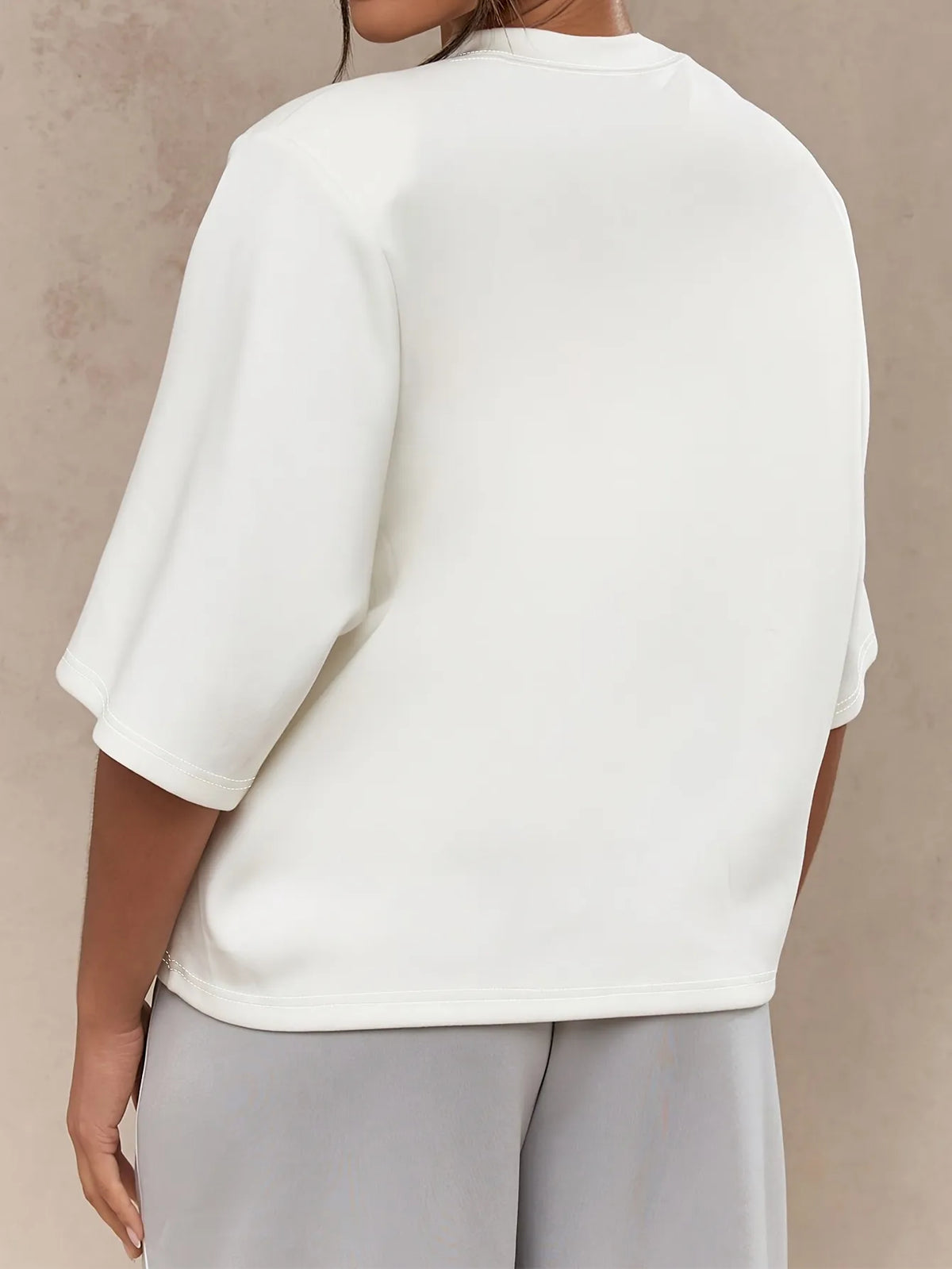 Person wearing a white blouse and light gray pants against a beige background